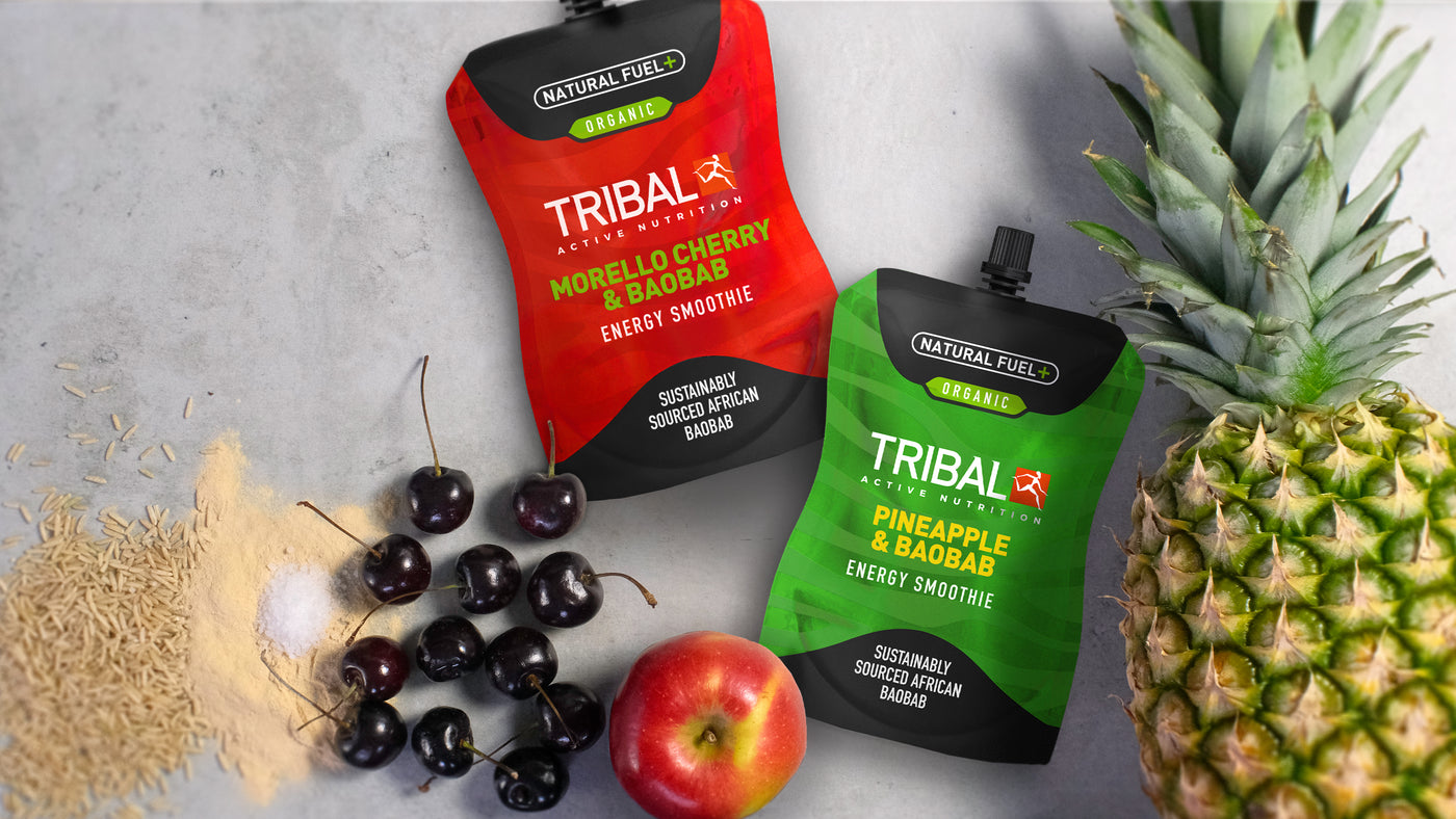 Two Tribal Active Energy Smoothies lying amongst a pineapple, apple, cherries, brown rice, baobab powder, and salt. On-the-go and performance nutrition. High in Vitamin C. Good for the gut. Natural and Organic. Sustainably sourced. GMO-Free